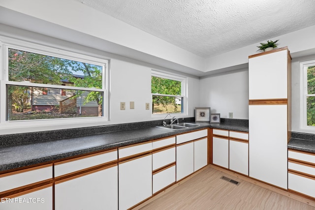 kitchen featuring white cabinetry, a textured ceiling, sink, and light wood-type flooring