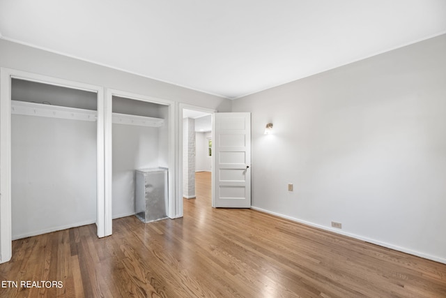 unfurnished bedroom featuring hardwood / wood-style flooring and multiple closets