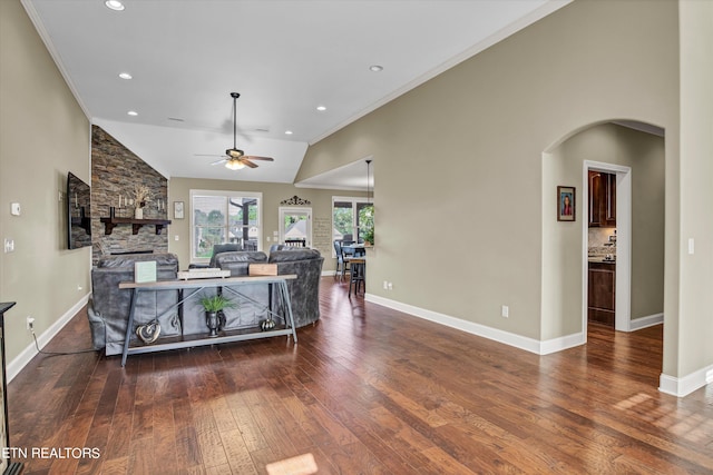 living room featuring ceiling fan, high vaulted ceiling, ornamental molding, dark wood-type flooring, and a stone fireplace