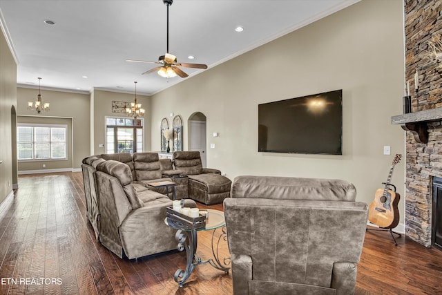 living room with crown molding, a stone fireplace, ceiling fan with notable chandelier, and dark hardwood / wood-style flooring