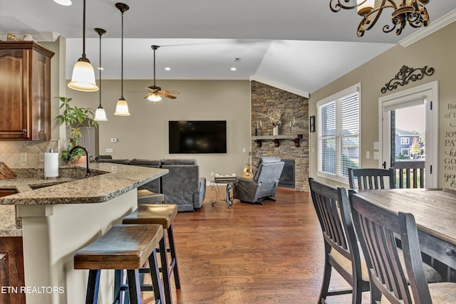 dining area with dark hardwood / wood-style floors, crown molding, vaulted ceiling, a fireplace, and ceiling fan with notable chandelier