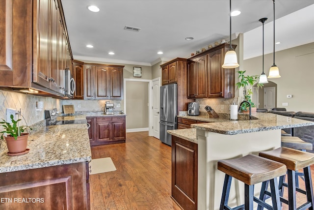 kitchen with appliances with stainless steel finishes, decorative light fixtures, decorative backsplash, a breakfast bar, and dark hardwood / wood-style floors