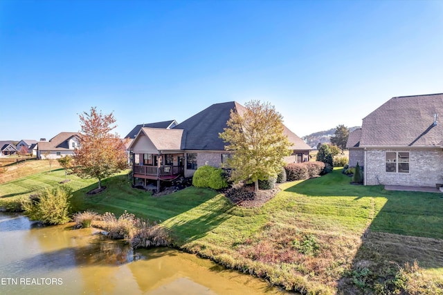 rear view of house with a deck with water view and a lawn