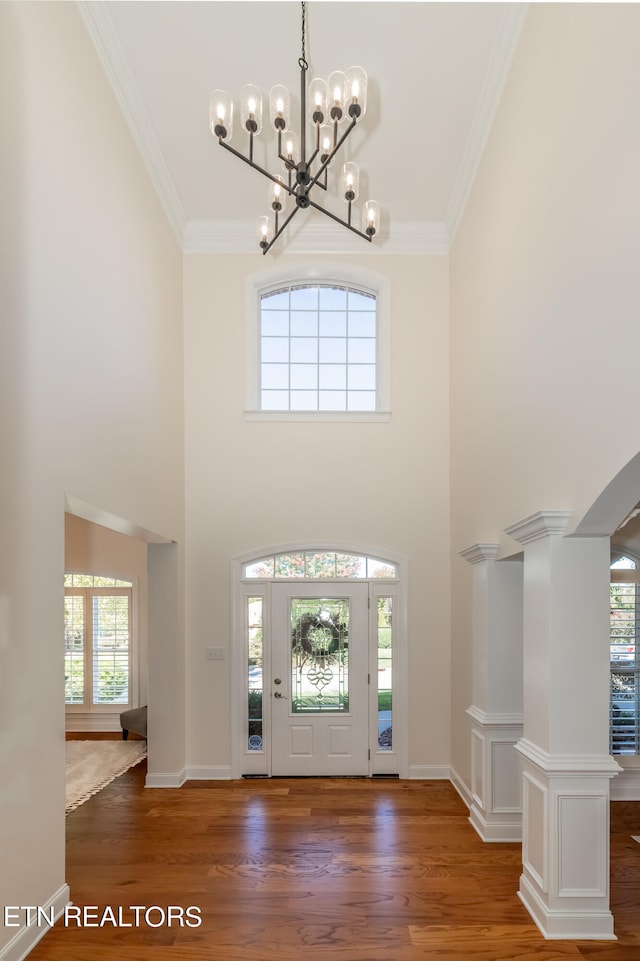 foyer with a towering ceiling, decorative columns, crown molding, a notable chandelier, and dark hardwood / wood-style floors