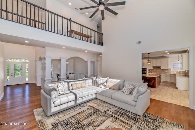 living room with ceiling fan, light wood-type flooring, a high ceiling, and decorative columns