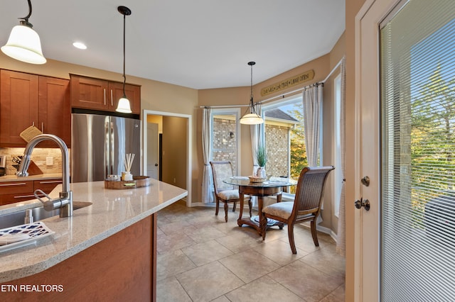 kitchen featuring stainless steel fridge, hanging light fixtures, light tile patterned flooring, sink, and light stone counters