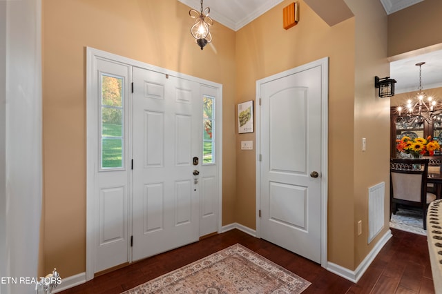 foyer entrance with dark wood-type flooring, crown molding, and a chandelier