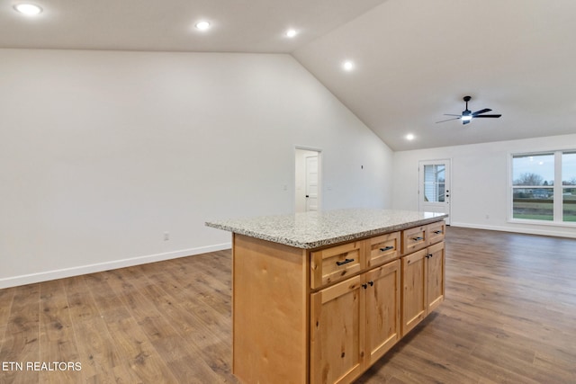 kitchen featuring hardwood / wood-style floors, a kitchen island, ceiling fan, and light stone counters