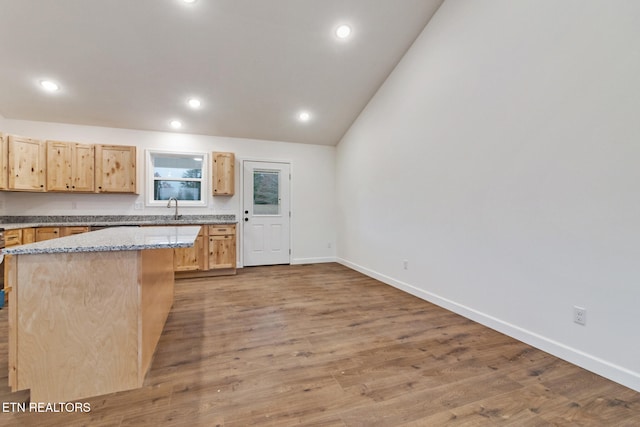 kitchen with a center island, sink, light stone counters, light hardwood / wood-style flooring, and lofted ceiling