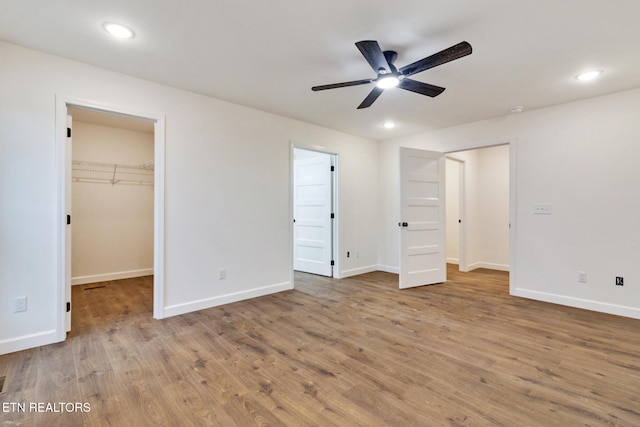 unfurnished bedroom featuring ceiling fan, a closet, a spacious closet, and light hardwood / wood-style flooring