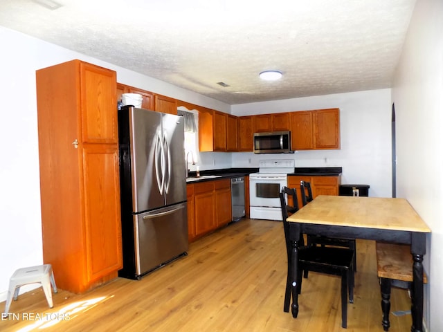 kitchen with sink, a textured ceiling, appliances with stainless steel finishes, and light hardwood / wood-style flooring