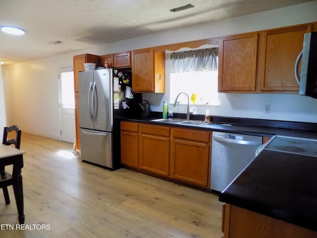 kitchen with a textured ceiling, appliances with stainless steel finishes, sink, and light wood-type flooring