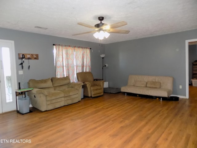 living room featuring light hardwood / wood-style floors, a textured ceiling, and ceiling fan