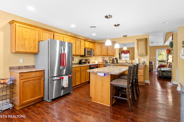 kitchen with a breakfast bar area, light countertops, appliances with stainless steel finishes, dark wood-style floors, and pendant lighting