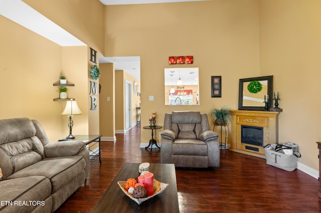 living room featuring dark wood-style flooring, a fireplace with raised hearth, a towering ceiling, and baseboards