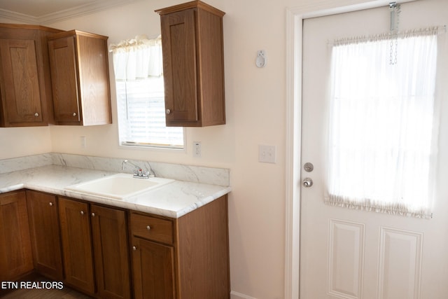 kitchen with light stone counters, ornamental molding, and sink