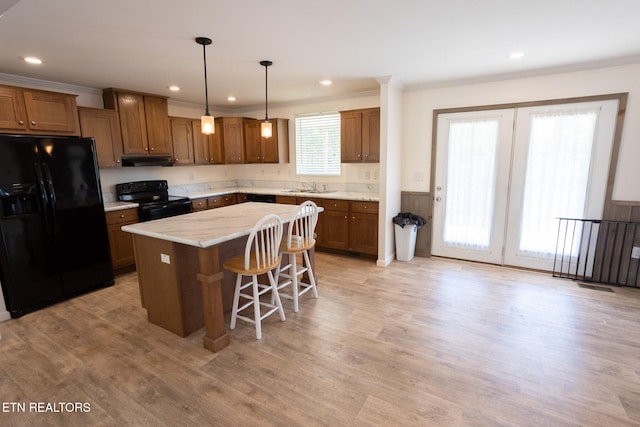 kitchen with a kitchen island, a kitchen breakfast bar, hanging light fixtures, sink, and black appliances