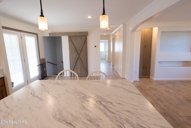 unfurnished dining area with crown molding, a barn door, a healthy amount of sunlight, and light wood-type flooring