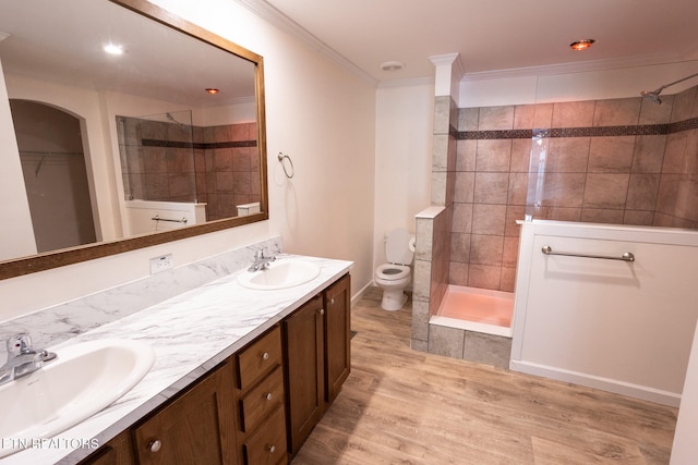 bathroom with wood-type flooring, toilet, tiled shower, vanity, and ornamental molding