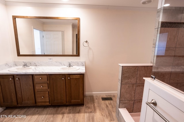 bathroom with vanity, crown molding, wood-type flooring, and tiled shower