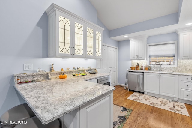 kitchen featuring dishwasher, decorative backsplash, a breakfast bar area, light wood-type flooring, and white cabinetry