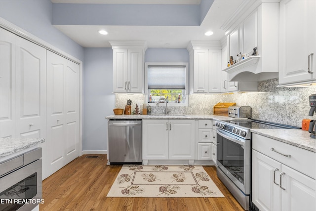 kitchen featuring light stone counters, white cabinetry, stainless steel appliances, and light wood-type flooring