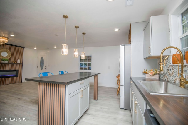 kitchen featuring a kitchen island, sink, light wood-type flooring, white refrigerator, and white cabinets