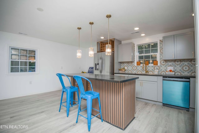 kitchen featuring appliances with stainless steel finishes, pendant lighting, gray cabinets, a center island, and light hardwood / wood-style floors