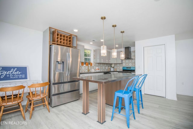 kitchen with decorative backsplash, wall chimney range hood, light hardwood / wood-style flooring, stainless steel appliances, and decorative light fixtures