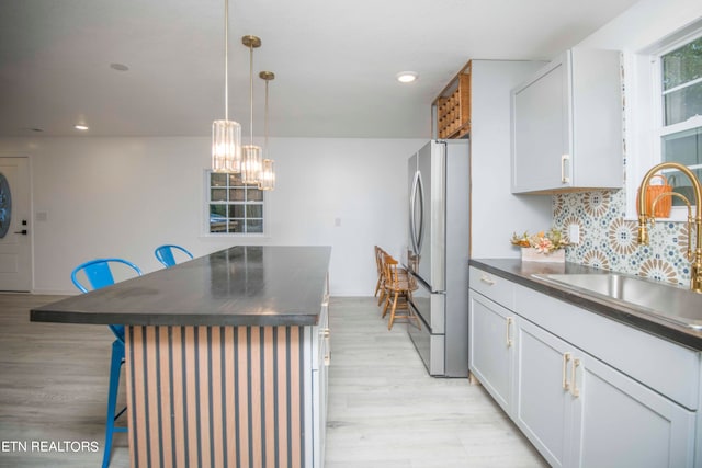 kitchen with a kitchen breakfast bar, stainless steel fridge, decorative light fixtures, white cabinets, and light hardwood / wood-style floors