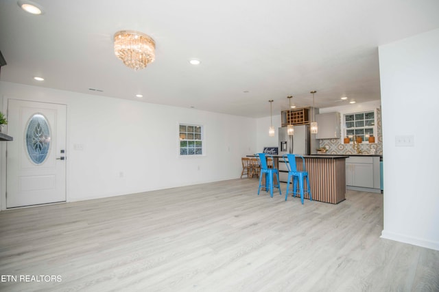 kitchen with gray cabinetry, backsplash, light hardwood / wood-style floors, a breakfast bar area, and stainless steel refrigerator with ice dispenser