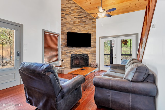 living room with french doors, ceiling fan, high vaulted ceiling, hardwood / wood-style floors, and a stone fireplace