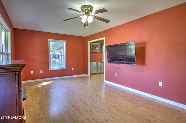 unfurnished living room with a wealth of natural light, radiator heating unit, light hardwood / wood-style floors, and ceiling fan