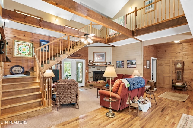 living room with a stone fireplace, beam ceiling, hardwood / wood-style flooring, and wooden walls