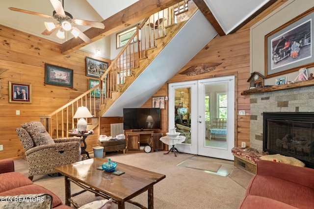 carpeted living room featuring beam ceiling, high vaulted ceiling, wood walls, a stone fireplace, and french doors