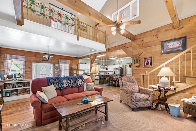 living room with beam ceiling, wooden walls, ceiling fan with notable chandelier, and light wood-type flooring