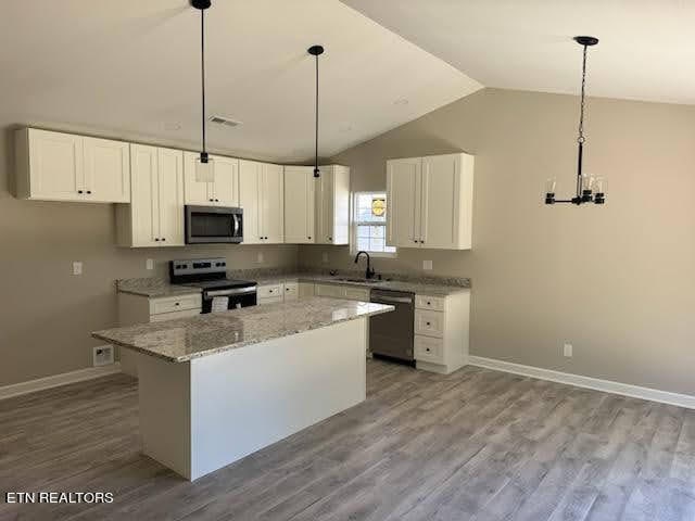 kitchen featuring light wood-type flooring, a kitchen island, stainless steel appliances, vaulted ceiling, and white cabinets