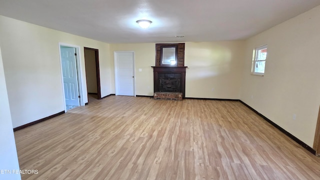 empty room featuring light wood finished floors, a fireplace, and baseboards