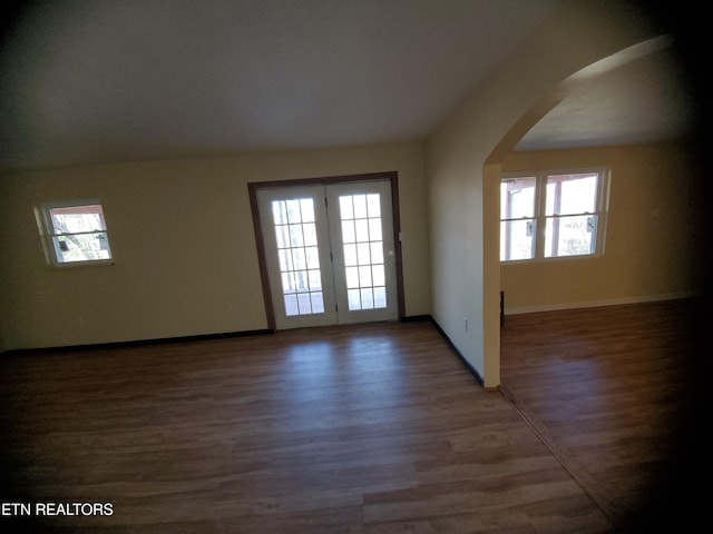 unfurnished room featuring arched walkways, baseboards, and wood finished floors