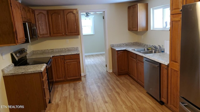 kitchen with brown cabinets, stainless steel appliances, light wood-type flooring, and a sink