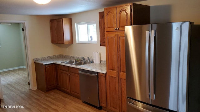 kitchen featuring light wood-style flooring, brown cabinetry, appliances with stainless steel finishes, and a sink