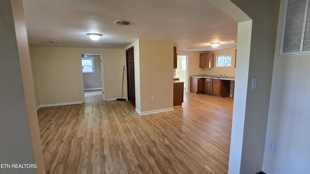 interior space featuring visible vents, baseboards, light wood-style flooring, arched walkways, and a sink