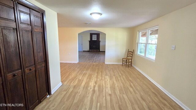 hall with baseboards, arched walkways, and light wood-style floors