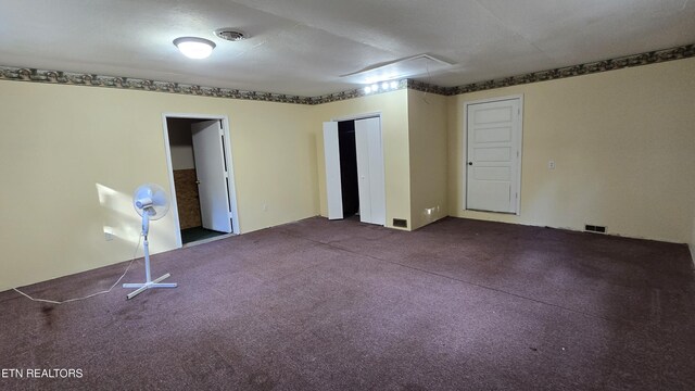 empty room featuring dark colored carpet, visible vents, and attic access