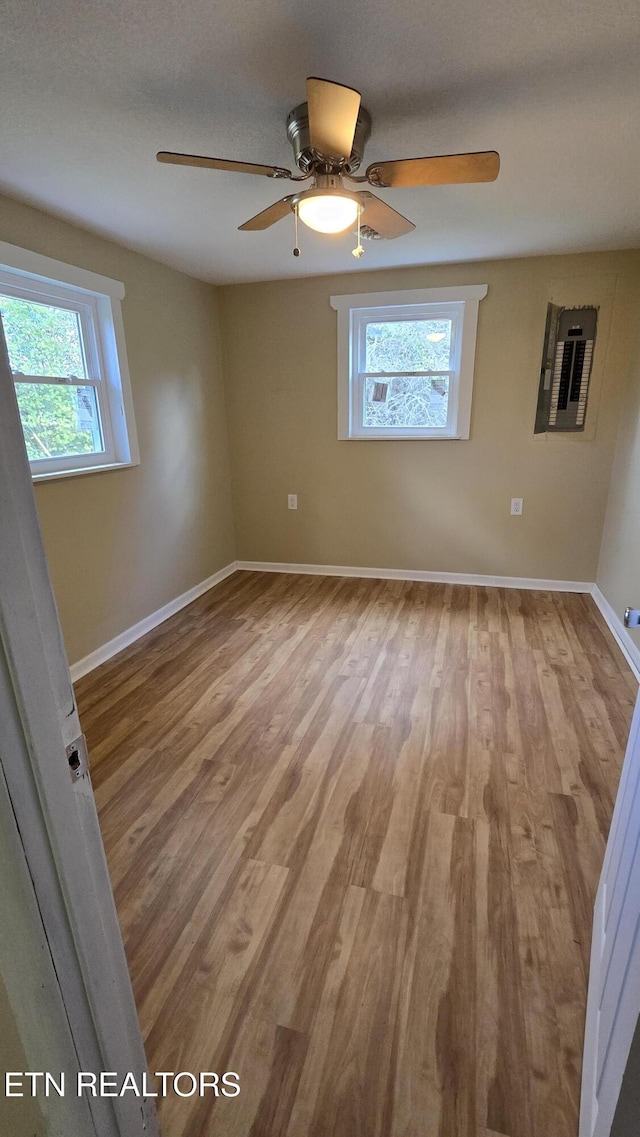 unfurnished room with electric panel, baseboards, and light wood-style floors