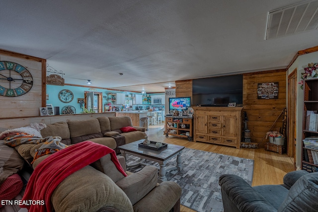 living room with a textured ceiling, light wood-type flooring, and wood walls