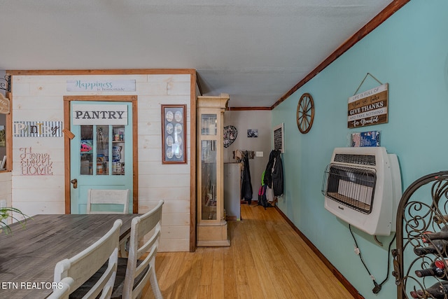 dining space with crown molding, heating unit, light hardwood / wood-style floors, and wood walls