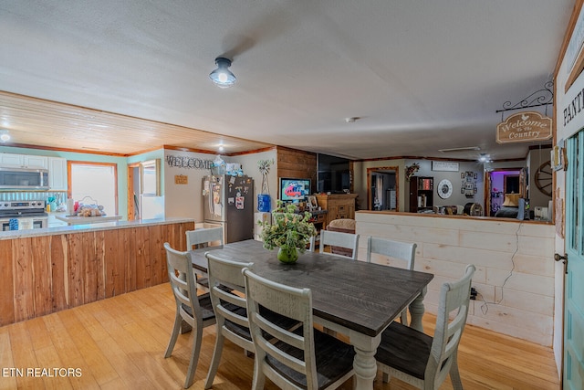 dining room with wooden walls, crown molding, light hardwood / wood-style floors, and ceiling fan