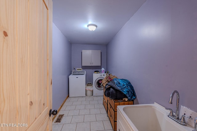 clothes washing area with sink, washer and dryer, light tile patterned floors, and cabinets