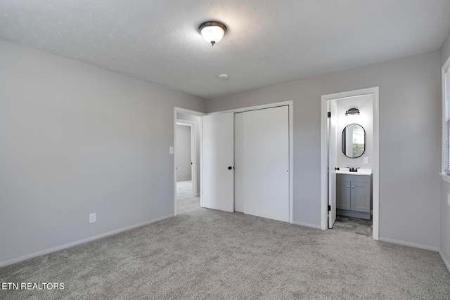 unfurnished bedroom with a closet, ensuite bathroom, light colored carpet, and sink